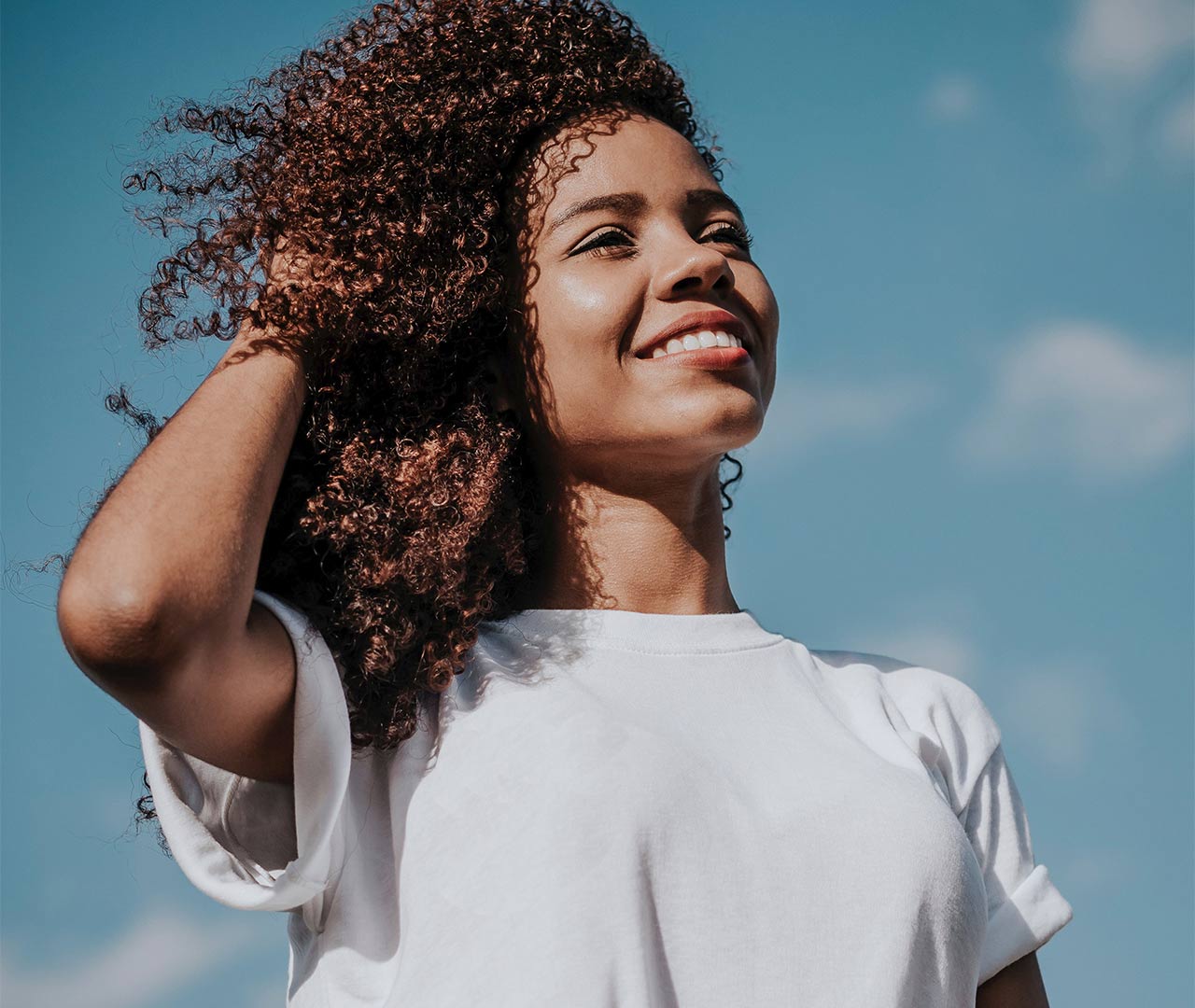 Woman smiling with blue sky and clouds behind her
